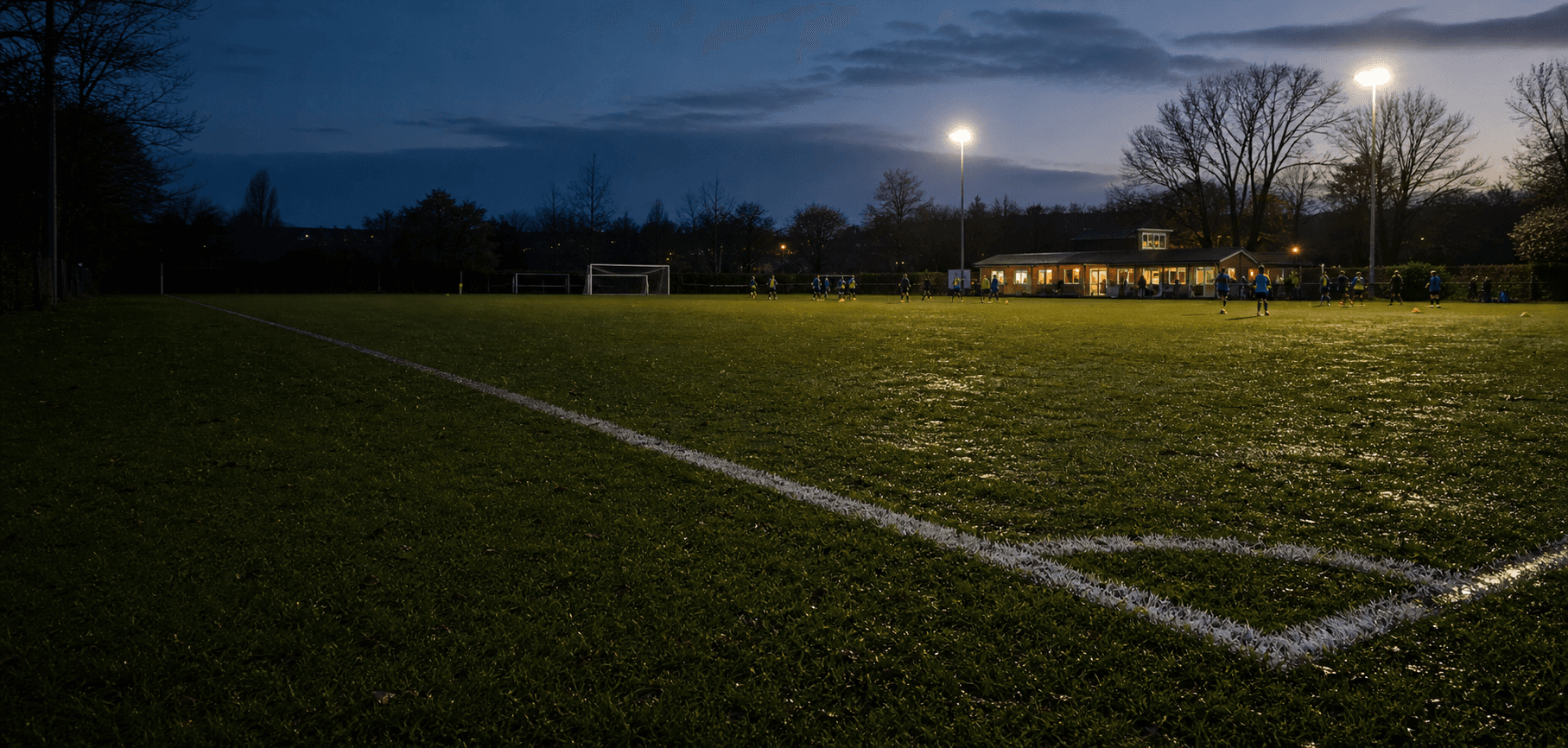 A floodlit grassroots football pitch at dusk